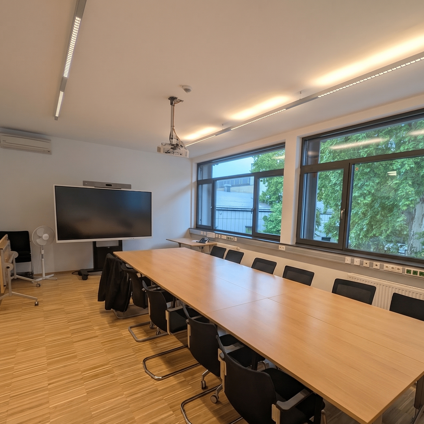 An empty conference room with a large screen, a projector, and a long table with chairs.