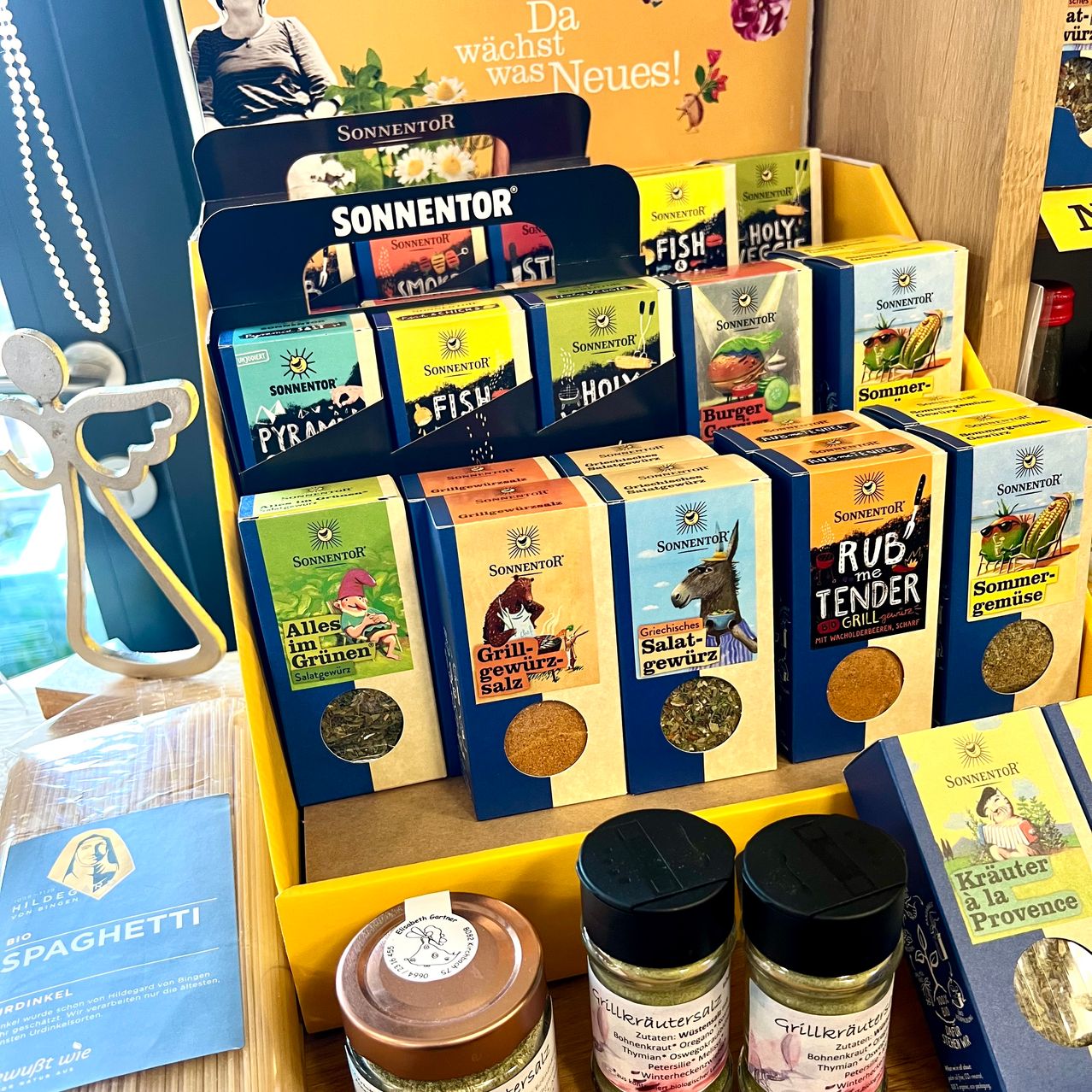 Eine Ausstellung verschiedener Gewürze und Würzmittel von Sonnentor. Mehrere kleine Verpackungen befinden sich in einer gelben Vitrine, mit anderen Gläsern und Würzmitteln in der Nähe.