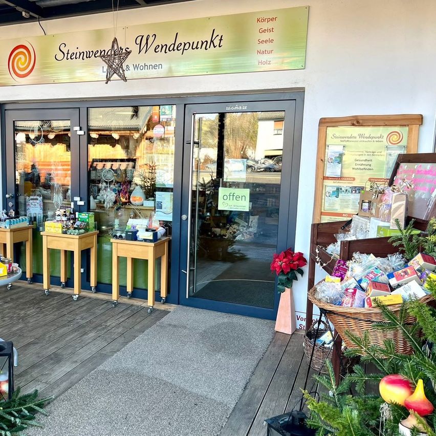Ein Geschäft namens Steinwenders Wendepunkt mit einer offenen Tür. Im Inneren sind mehrere ausgestellte Artikel. Draußen befinden sich auch Pflanzen und Weihnachtsdekorationen.