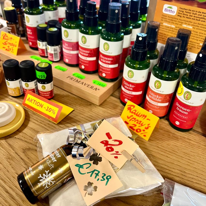 Auf einem Holztisch sind verschiedene ätherische Ölsprays mit Preisschildern ausgestellt. Die Produkte sind in Reihen mit gelben und roten Etiketten angeordnet. Ein Produkt hat ein Preisschild für 10% Rabatt.