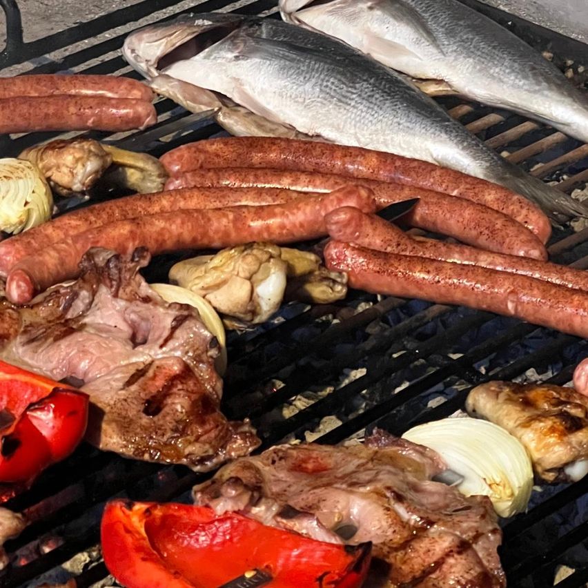 Ein Grill mit verschiedenen Fleischsorten, Würsten, Fisch und Gemüse wie Paprika und Zwiebeln, die alle gekocht werden.
