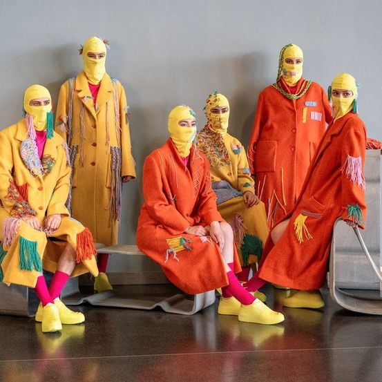 Eine Gruppe von Menschen in hellen gelben und orangefarbenen Kostümen mit gelben Masken posiert für ein Foto in einem Raum.