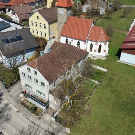 Luftaufnahme einer Kleinstadt mit verschiedenen Häusern, einer Kirche und grünen Feldern. Mehrere Häuser haben Solarpanels.