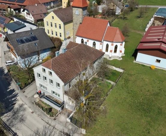 Luftaufnahme einer Kleinstadt mit verschiedenen Häusern, einer Kirche und grünen Feldern. Mehrere Häuser haben Solarpanels.
