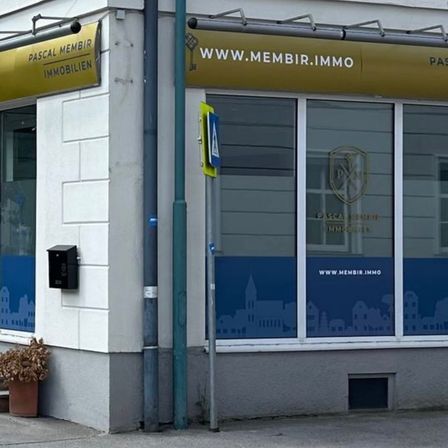 Das Äußere eines Gebäudes mit einem Schild, das Pascal Membrir Immobilien sagt. Es gibt Topfpflanzen auf dem Bürgersteig.