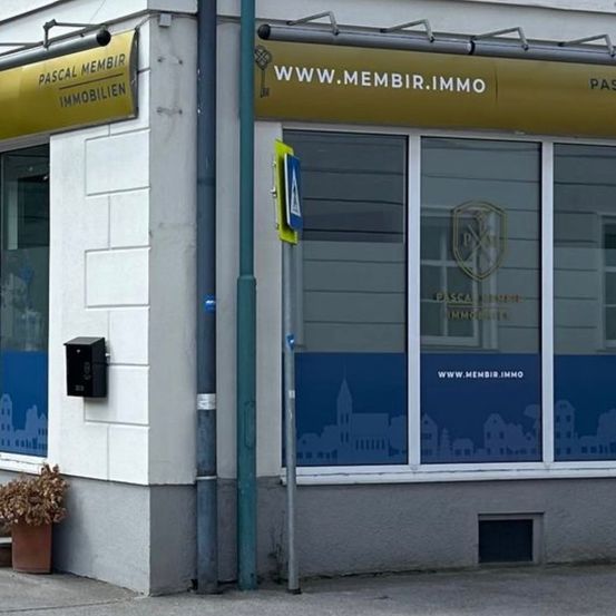 Das Äußere eines Gebäudes mit einem Schild, das Pascal Membrir Immobilien sagt. Es gibt Topfpflanzen auf dem Bürgersteig.