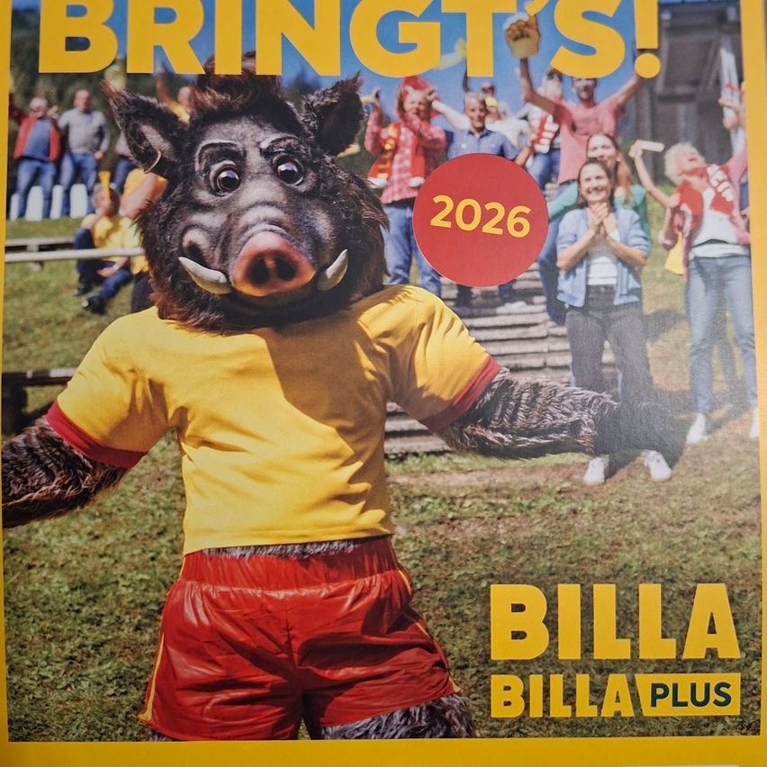 A mascot in a pig costume stands with yellow shirt and red shorts, surrounded by cheering people and a 2026 circle.