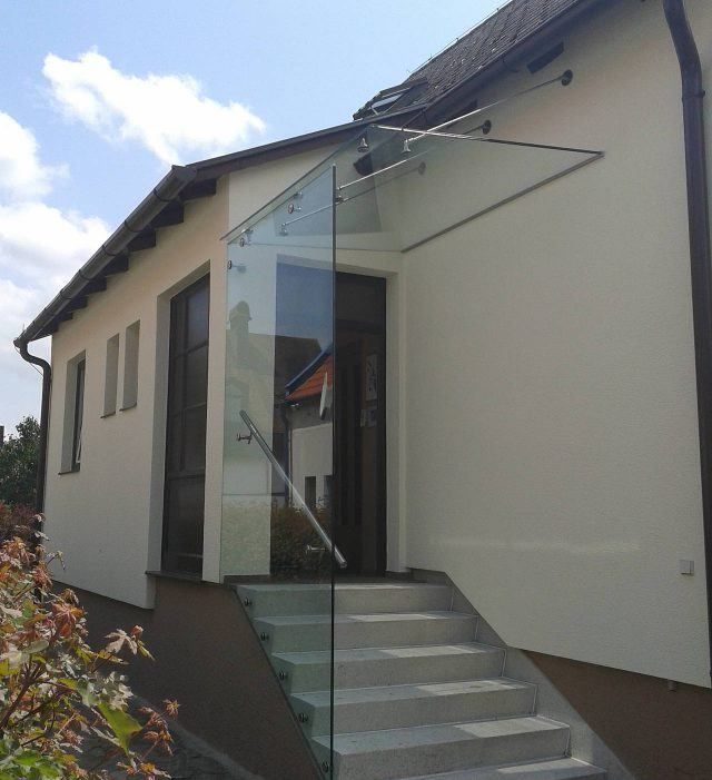Außenansicht eines modernen Hauses mit Glasstufen und einem Glasvordach über dem Eingang.