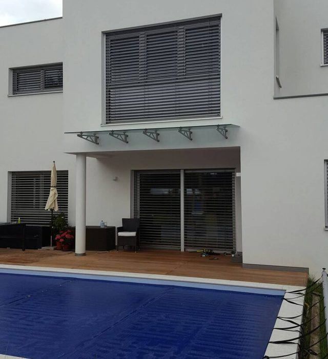 Ein modernes weißes Haus mit Pool, Holzterrasse und einer Glasüberdachung über dem Eingang.