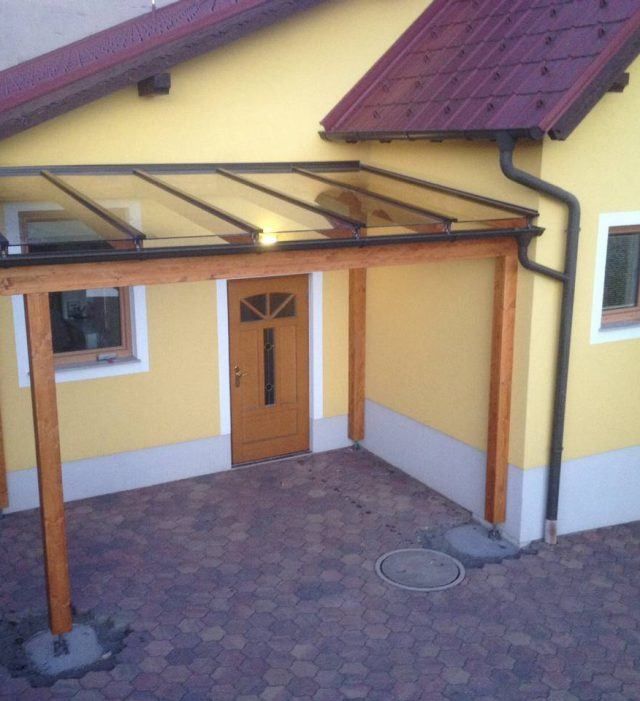 Ein gelbes Haus mit einer Glasüberdachung und einer Holztür an der Seite.
