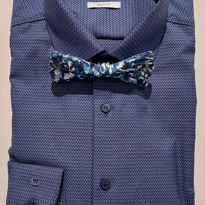 Ein marineblaues Hemd mit Fischgrätmuster und einer floralen Fliege zur Schau gestellt. Das Hemd hat einen Knopfleistenkragen und eine Brusttasche.