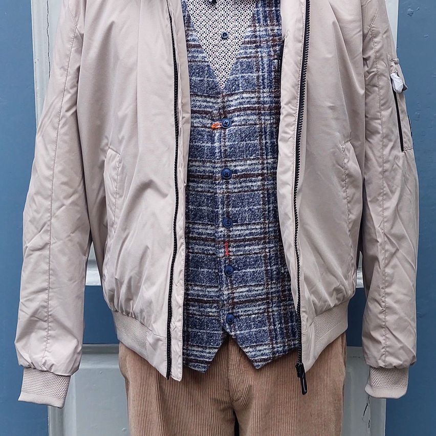 A mannequin wearing a beige bomber jacket over a blue plaid shirt and brown corduroy pants.