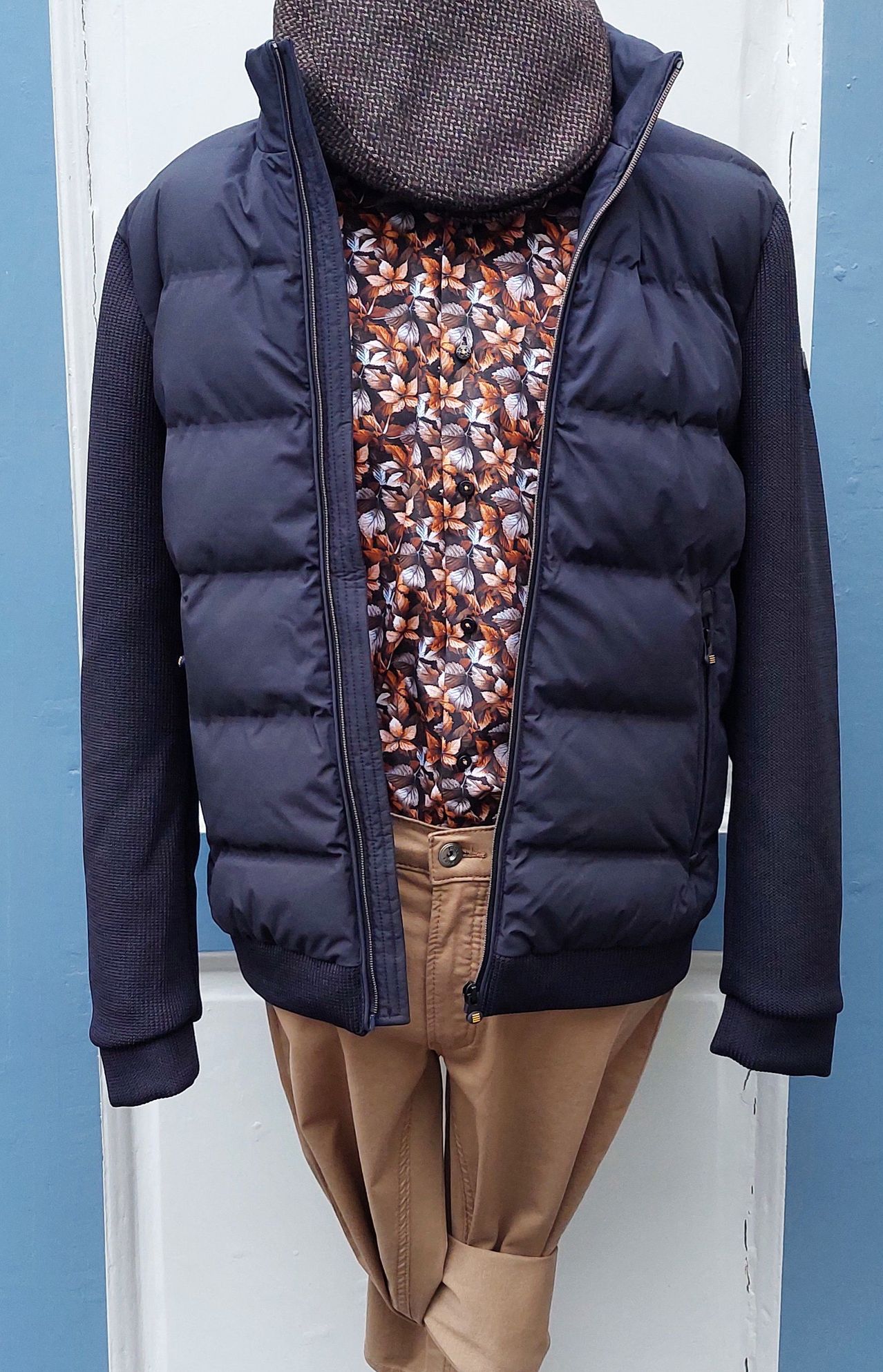 A navy blue puffer jacket with a floral shirt underneath, displayed against a light blue background.