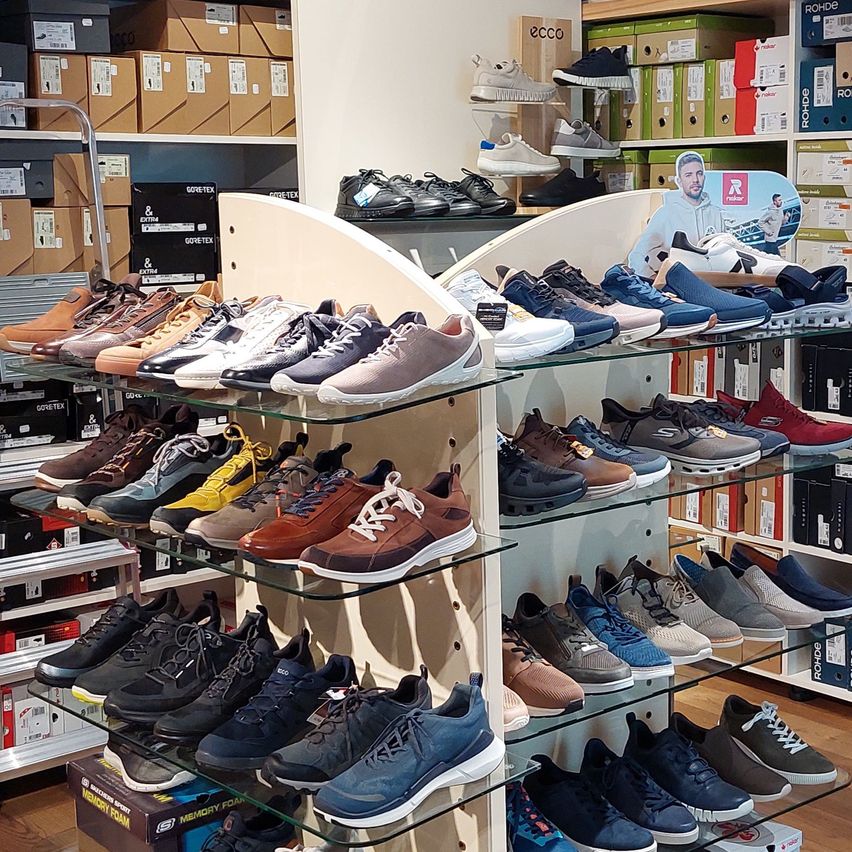 A shoe shop with a variety of sneakers displayed on glass shelves, including running shoes, loafers, and casual shoes. Boxes and storage boxes are placed behind the shelves.