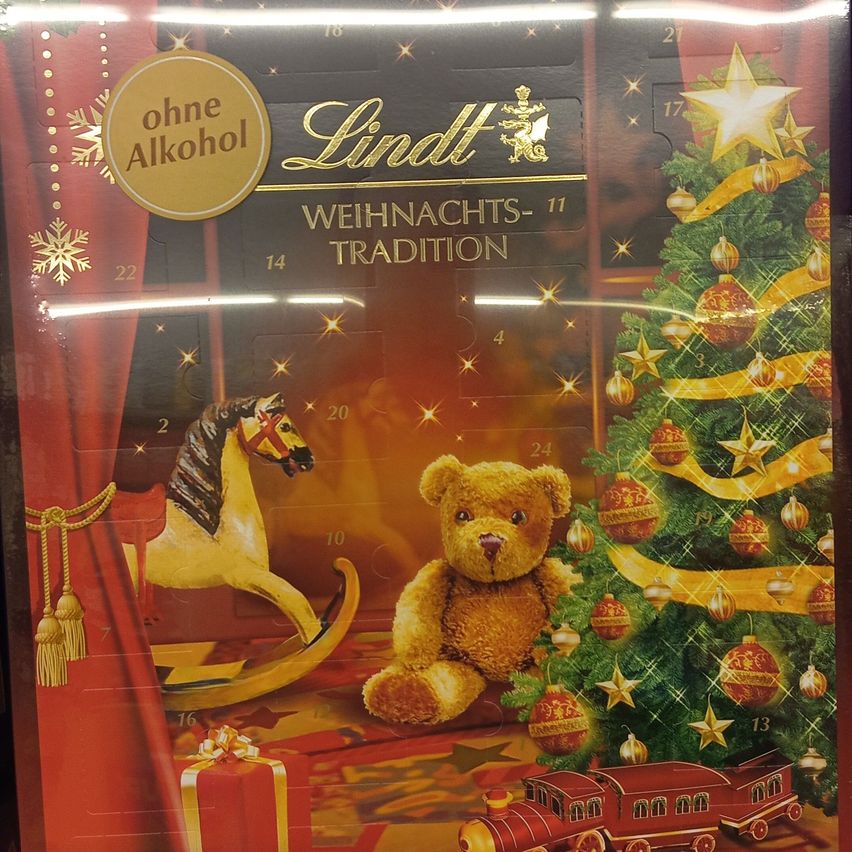 Ein Lindt-Weihnachtskalender mit einem Teddybär, einem Schaukelpferd und einem Weihnachtsbaum. Er zeigt einen goldenen Stern oben auf dem Baum und ein Geschenk darunter.