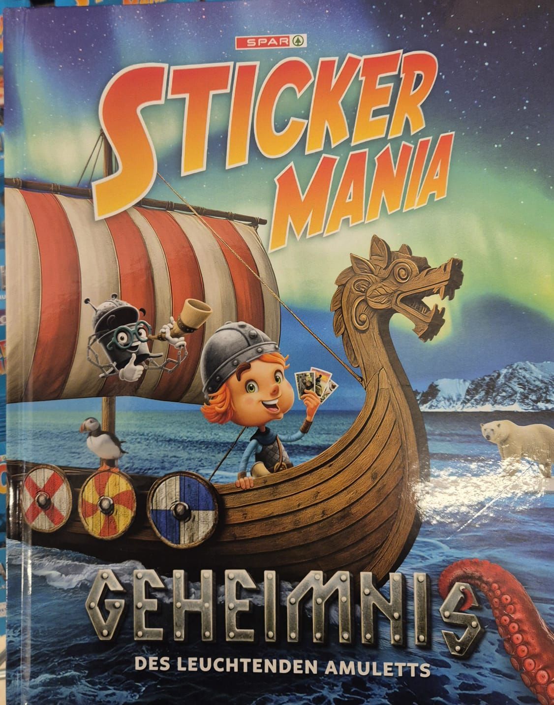 Buchcover mit Wikinger-Thema. Ein Mädchen hält ein Kartenspiel und ein Roboter sitzt neben ihr. Ein Drachenkopf schmückt den Bug des Wikingerschiffs.