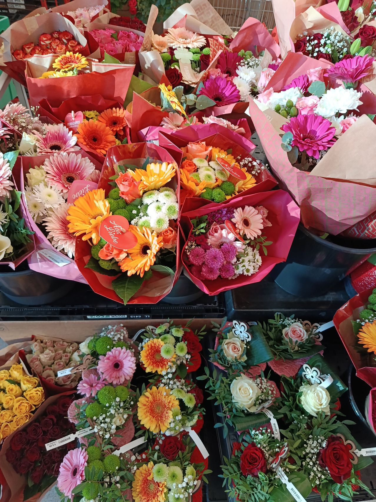 Eine Sammlung von bunten Blumensträußen in rosa und roten Verpackungen mit verschiedenen Blumen wie Gänseblümchen und Rosen, auf einem Tresen ausgestellt.