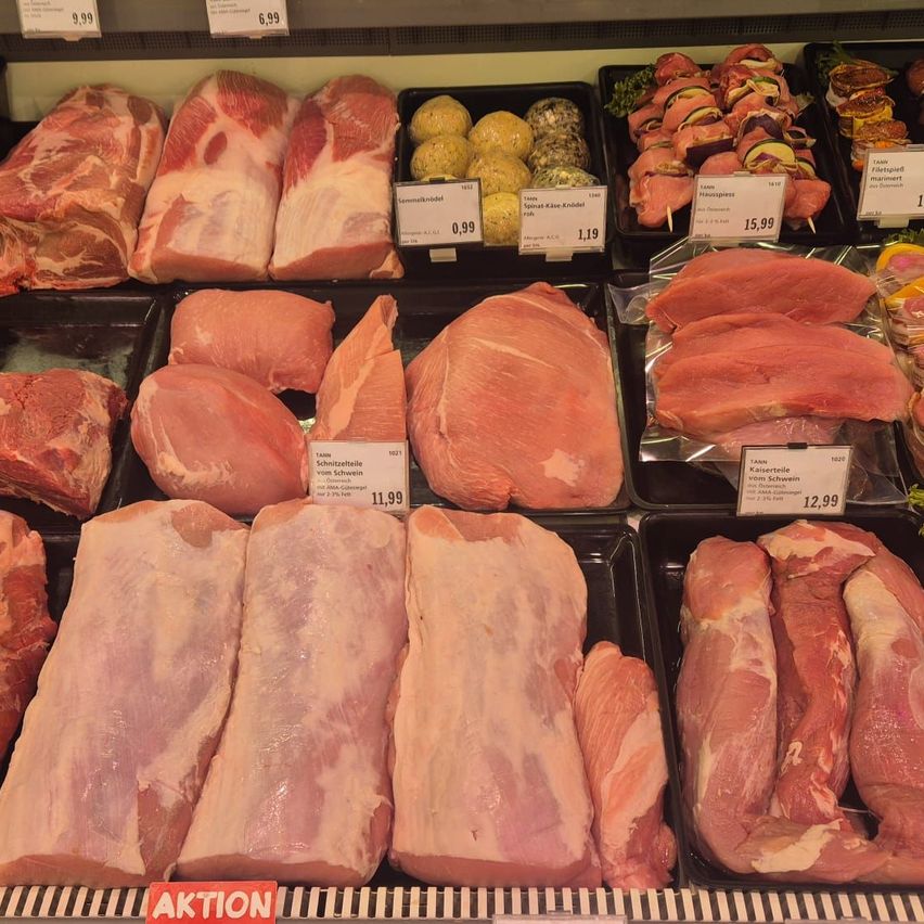 Ein Fleischregal in einem Supermarkt zeigt verschiedene Schweinefleischsorten und Würste. Die Preise sind auf Preisschildern angegeben.