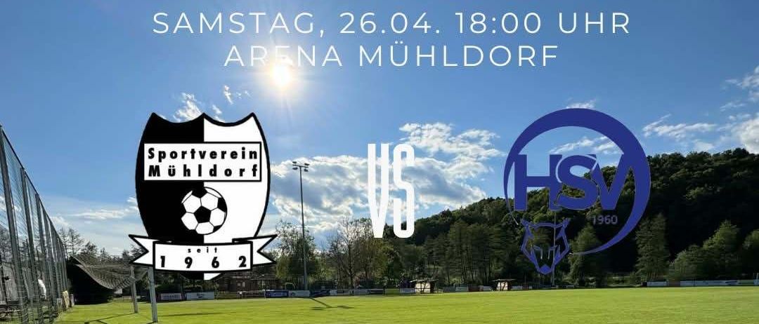 Heimspiel am Samstag, 26. April, um 18:00 Uhr in der Arena Mühldorf. Das Fußballfeld ist von einem Zaun umgeben, und die Sonne scheint.