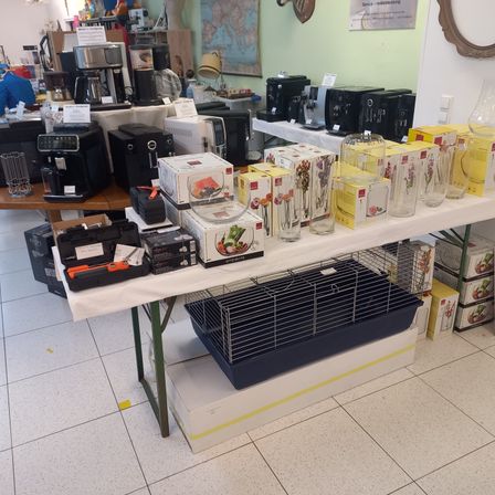 Ein Raum voller verschiedener elektronischer Geräte und Kisten, darunter ein schwarzer Kaninchenkäfig auf einem weißen Tisch.