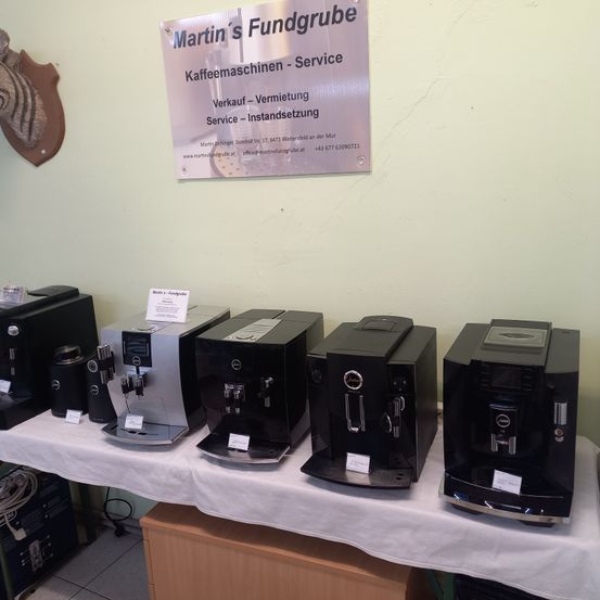 Eine Ausstellung mehrerer schwarzer und silberner Kaffeemaschinen auf einem Tisch mit einem Schild, das Martin's Fundgrube Kaffeemaschinen - Service liest.