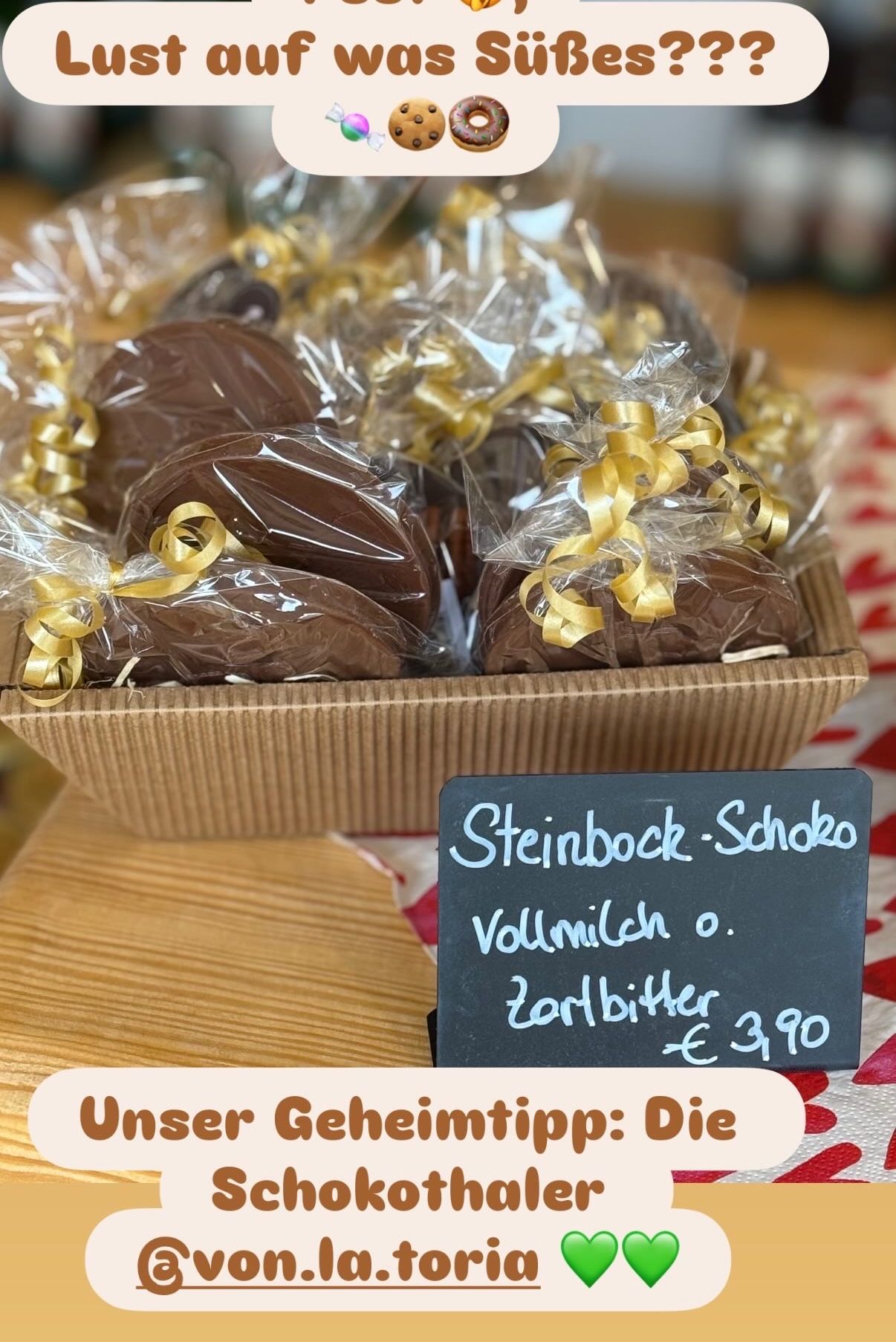 Eine Schachtel Schokoladen, verpackt in Plastik mit goldenen Schleifen. Ein Tafel mit dem Text Steinbock-Schokolade, Vollmilch oder Zartbitter, und einem Preis von 3,90 Euro.