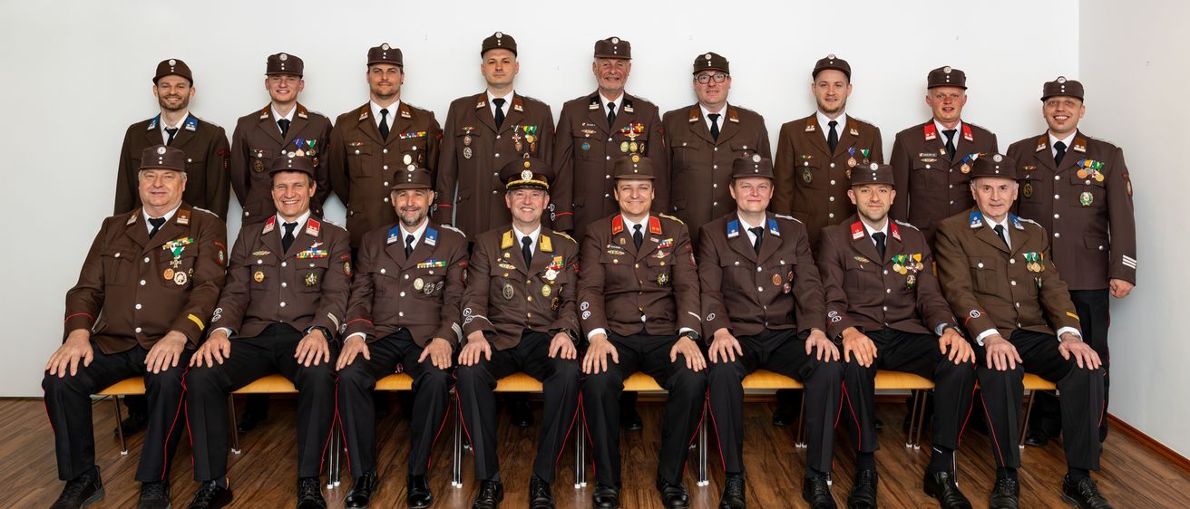 Eine Gruppe von Militäroffizieren in braunen Uniformen mit Medaillen und Abzeichen, die auf einer Bank sitzen und für ein Foto posieren.