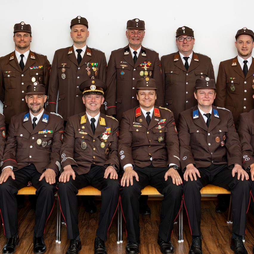 Eine Gruppe von Militäroffizieren in braunen Uniformen mit Medaillen und Abzeichen, die auf einer Bank sitzen und für ein Foto posieren.
