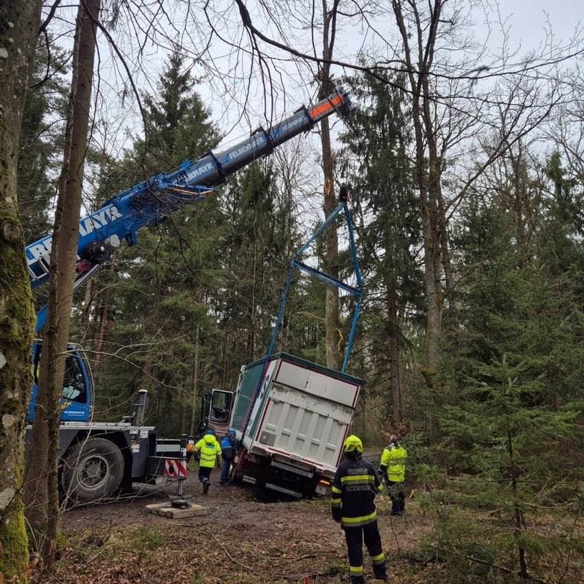 Ein Kran hebt einen in einem Waldgebiet feststeckenden Lkw, mit Personal in Schutzausrüstung in der Nähe.
