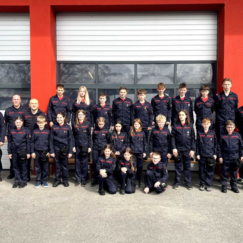 A group of students and instructors in blue uniforms are posing for a photo in front of a red building with glass windows.