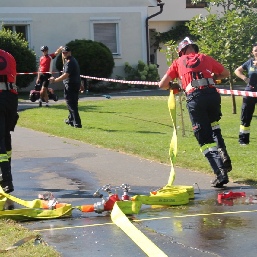 Feuerwehrleute üben mit Schläuchen auf einem nassen Bürgersteig vor einem Gebäude.