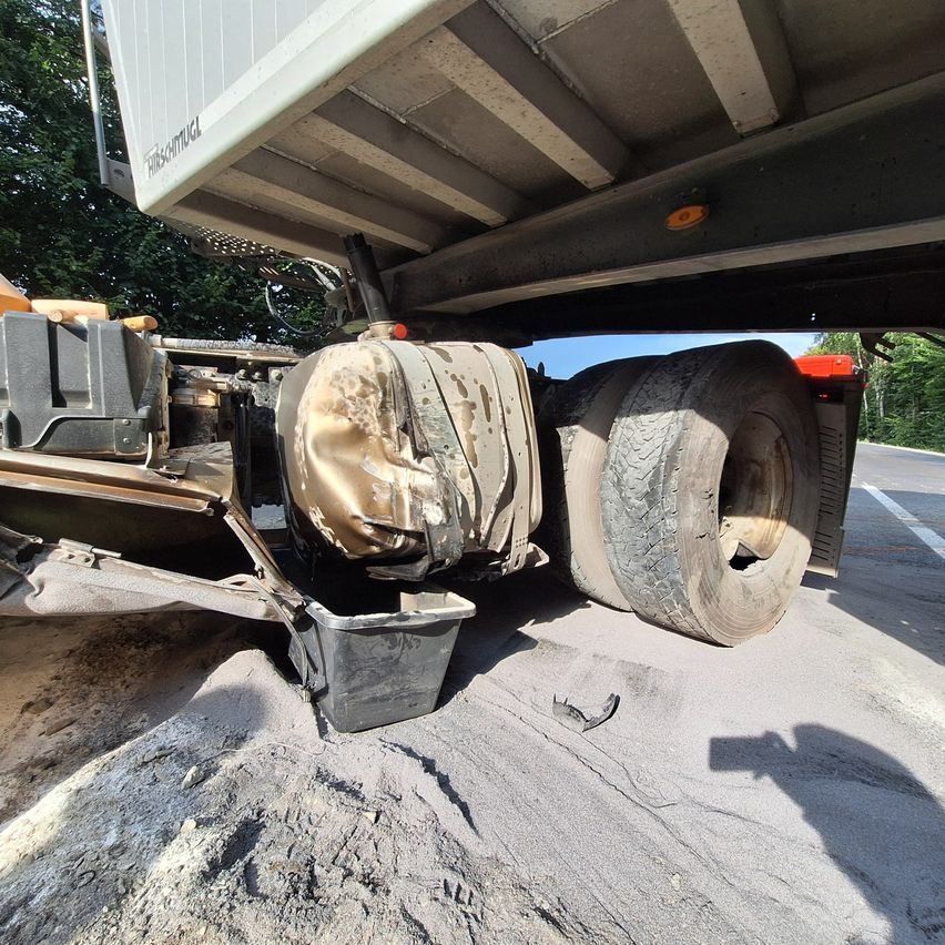 A damaged truck with a burnt component on the back, parked on the side of the road with a shadow cast on the ground.