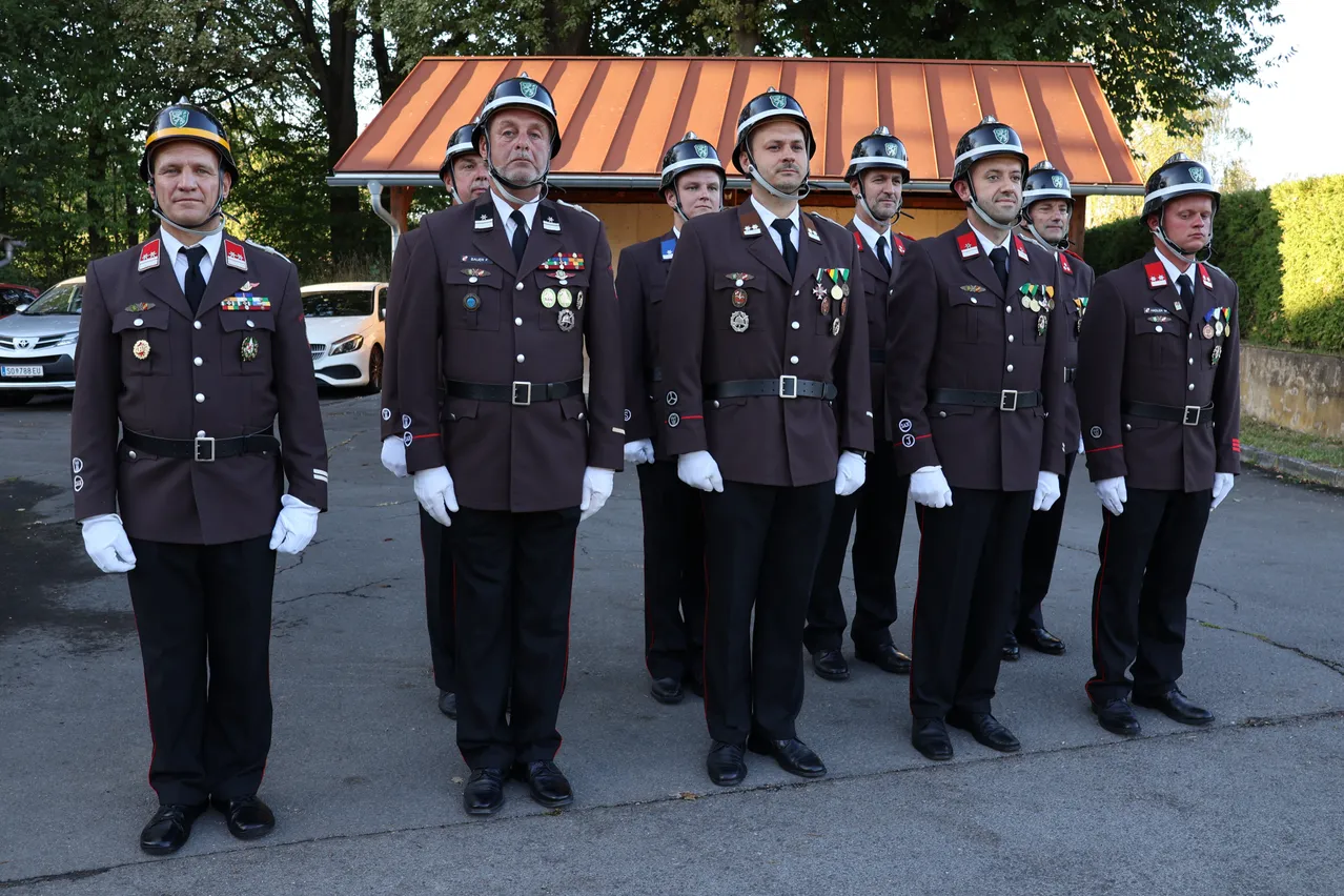 Eine Gruppe uniformierter Beamter, möglicherweise Polizisten, steht in einer Reihe vor einem Gebäude. Sie tragen Helme, Krawatten und Handschuhe.