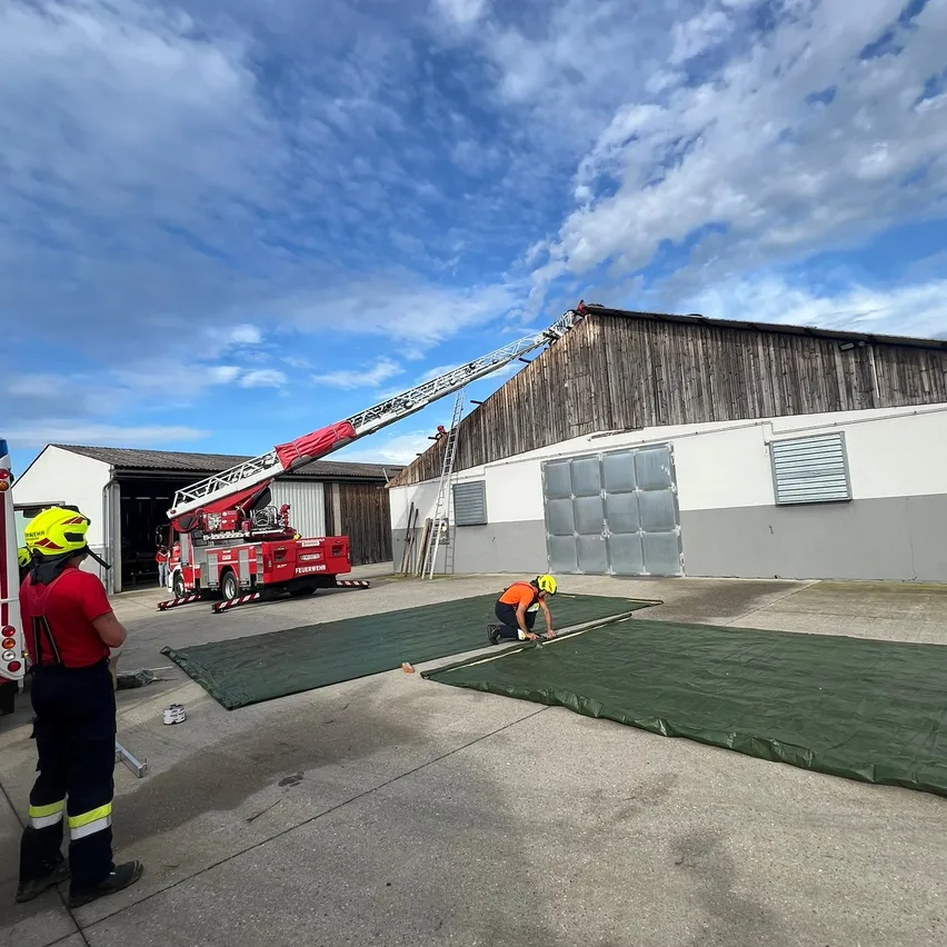 Feuerwehrleute bereiten einen Feuerwehrwagen an einem sonnigen Tag vor. Ein Feuerwehrmann ist auf der Leiter, während ein anderer am Boden arbeitet.