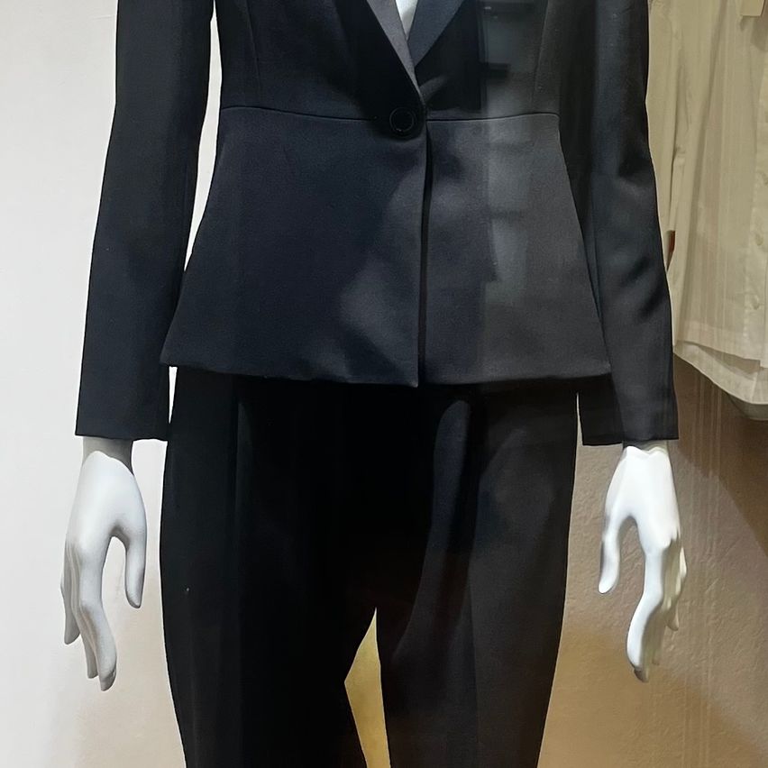Ein Mannequin zeigt einen schwarzen Anzug mit einem einzelnen Knopf am Jackett. Der Anzug besteht aus einem taillierten Jackett mit hohem Kragen und Hosen.