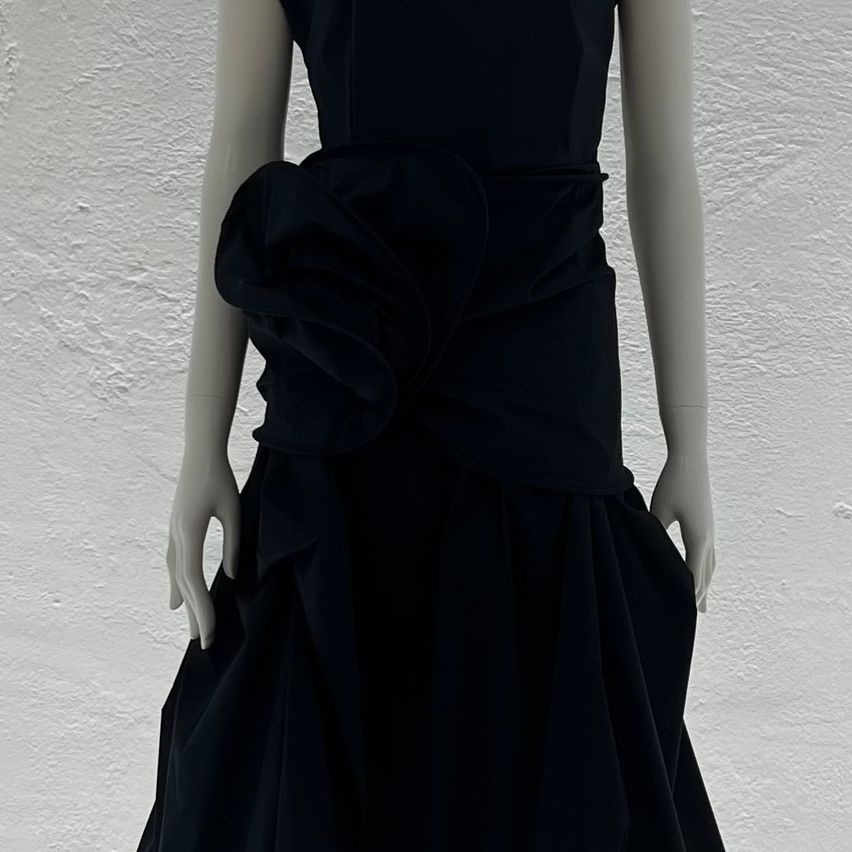 A mannequin displays a black evening gown with an elegant ruffled design at the waist and flowing skirt.