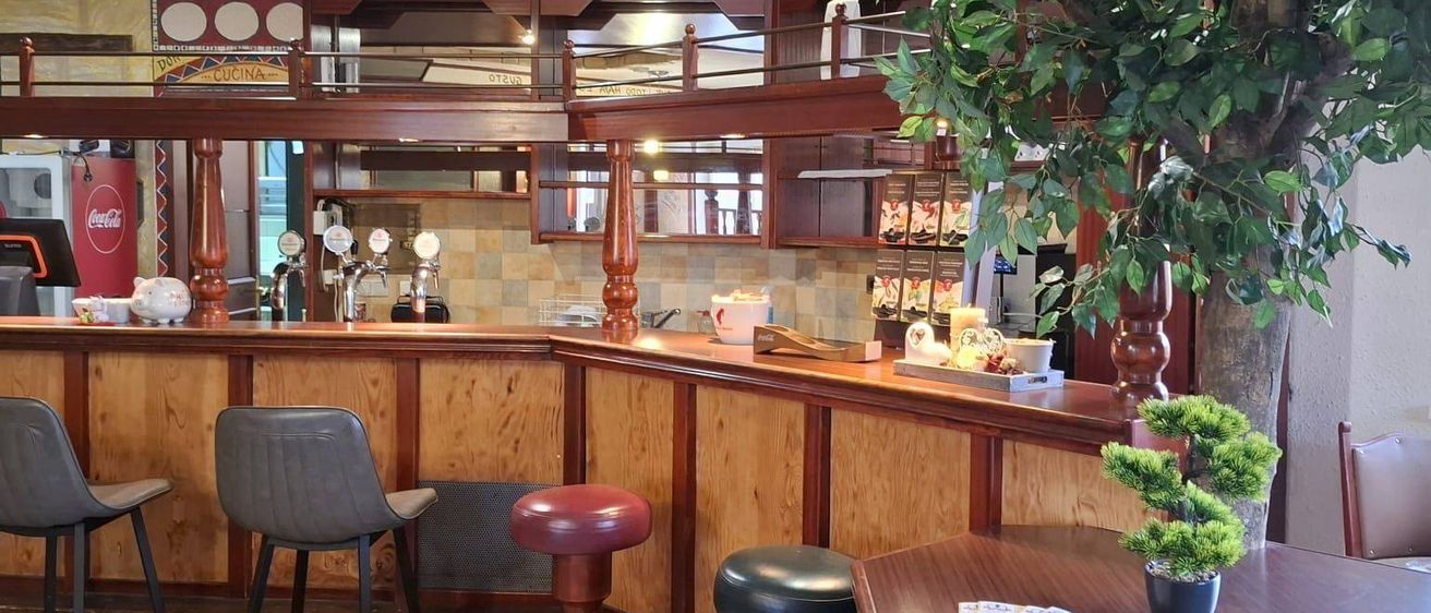 Ein leerer Barbereich mit Holztheke und Hockern sowie einem Baum auf der rechten Seite.