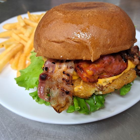Ein Burger mit Speck, gebratenem Huhn und Käse auf einem weißen Teller mit Pommes frites serviert.