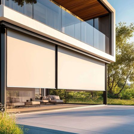 Modernes Haus mit Glaswänden, Balkon und rollbaren Sonnenschutzrollos. Im Inneren Lounge-Sessel und Tische auf einer Terrasse. Bäume und Gras im Hintergrund.