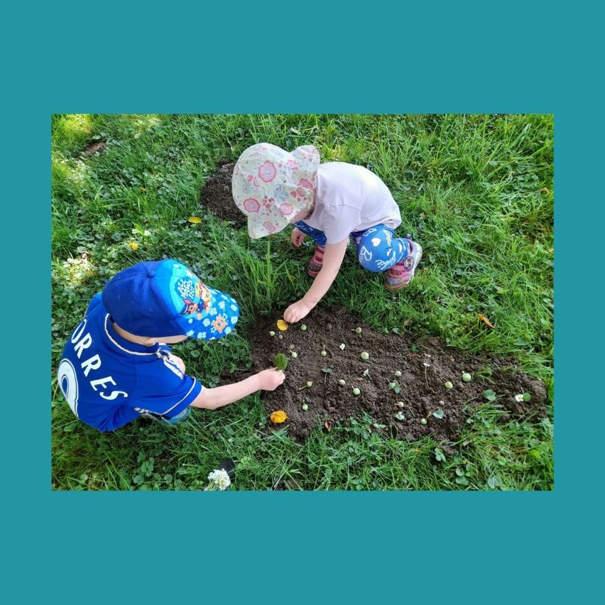 Zwei Kinder pflanzen Samen im Garten. Ein Kind trägt ein blaues Shirt mit dem Wort 'Corres' darauf. Das andere Kind trägt ein rosa Shirt.