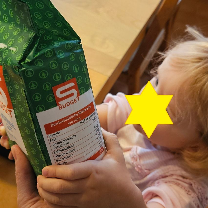 A toddler holds a bag of cereal with a yellow star. The cereal bag is green with white text and shows nutritional information.