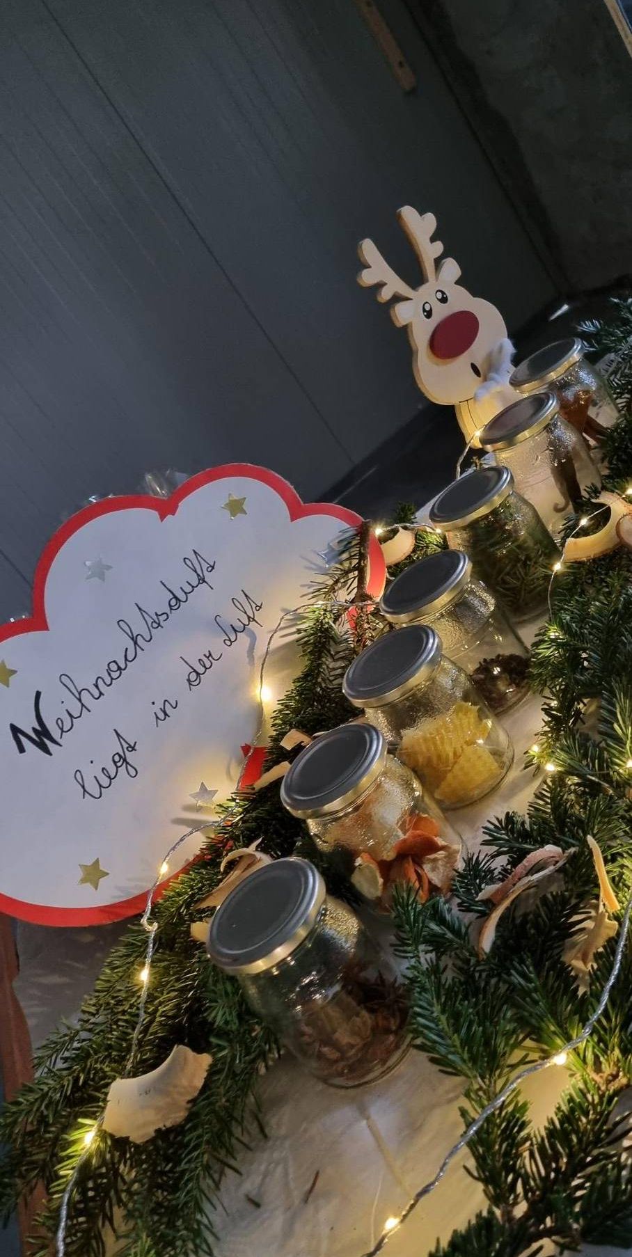 Ein Weihnachtstisch mit Gläsern verschiedenen Inhalts, einem herzförmigen Schild, einem beleuchteten Weihnachtsbaum und einer Weihnachtsmann-Figur.