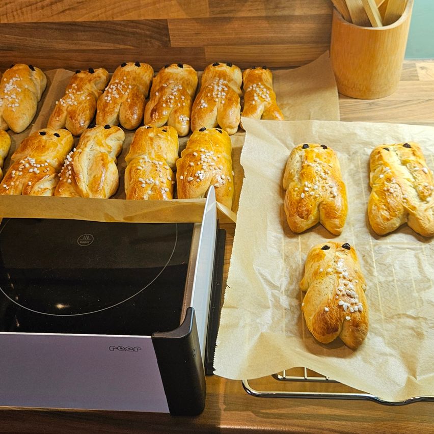 Ein Tisch mit mehreren Tabletts mit Gebäck, darunter schokoladengefüllte Pasteten, angeordnet auf Backpapier und kühlt auf einem Rost. Ein elektronisches Gerät ist in der Nähe.