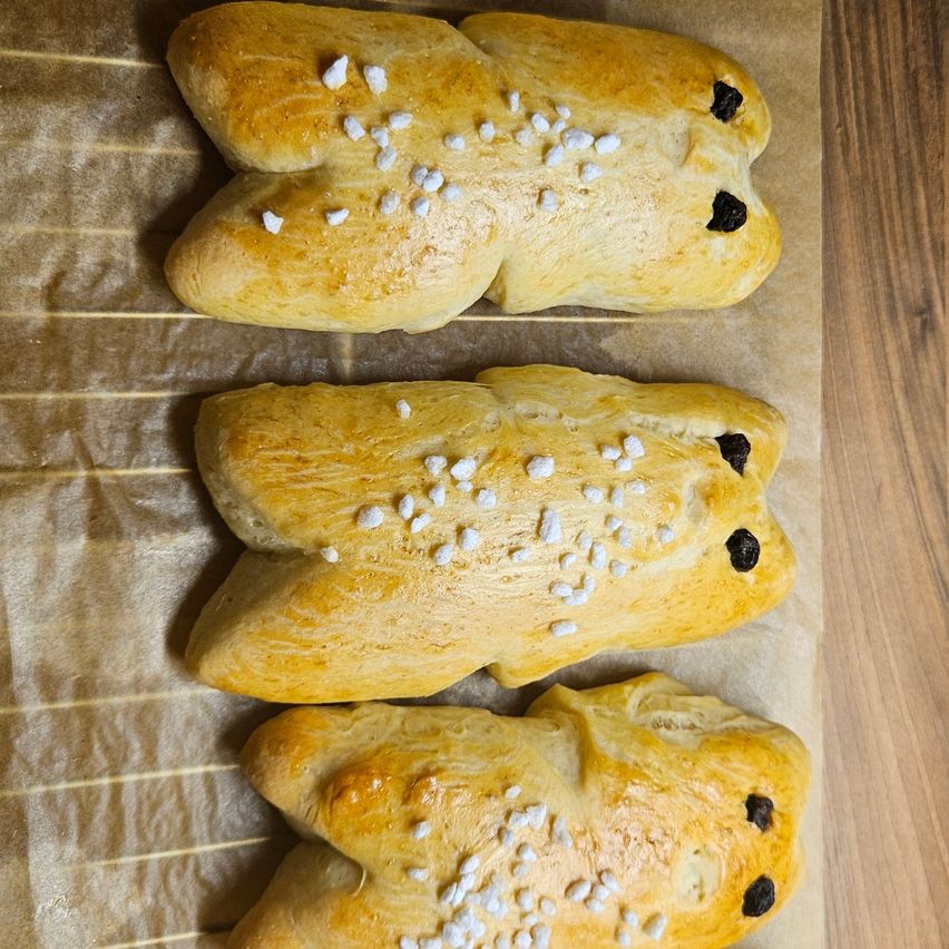 Drei goldbraune, bärenförmige Gebäckstücke mit weißen und schwarzen Streuseln sind auf einem Backpapier angeordnet.