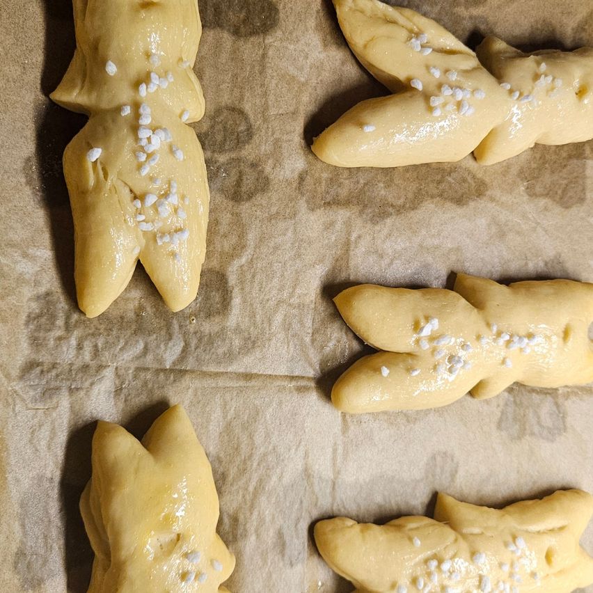 Sechs teigförmige Häschen, jedes mit weißem Zucker bestreut, liegen auf Backpapier und sind bereit zum Backen. Sie haben kleine Ohren und Schwänze.