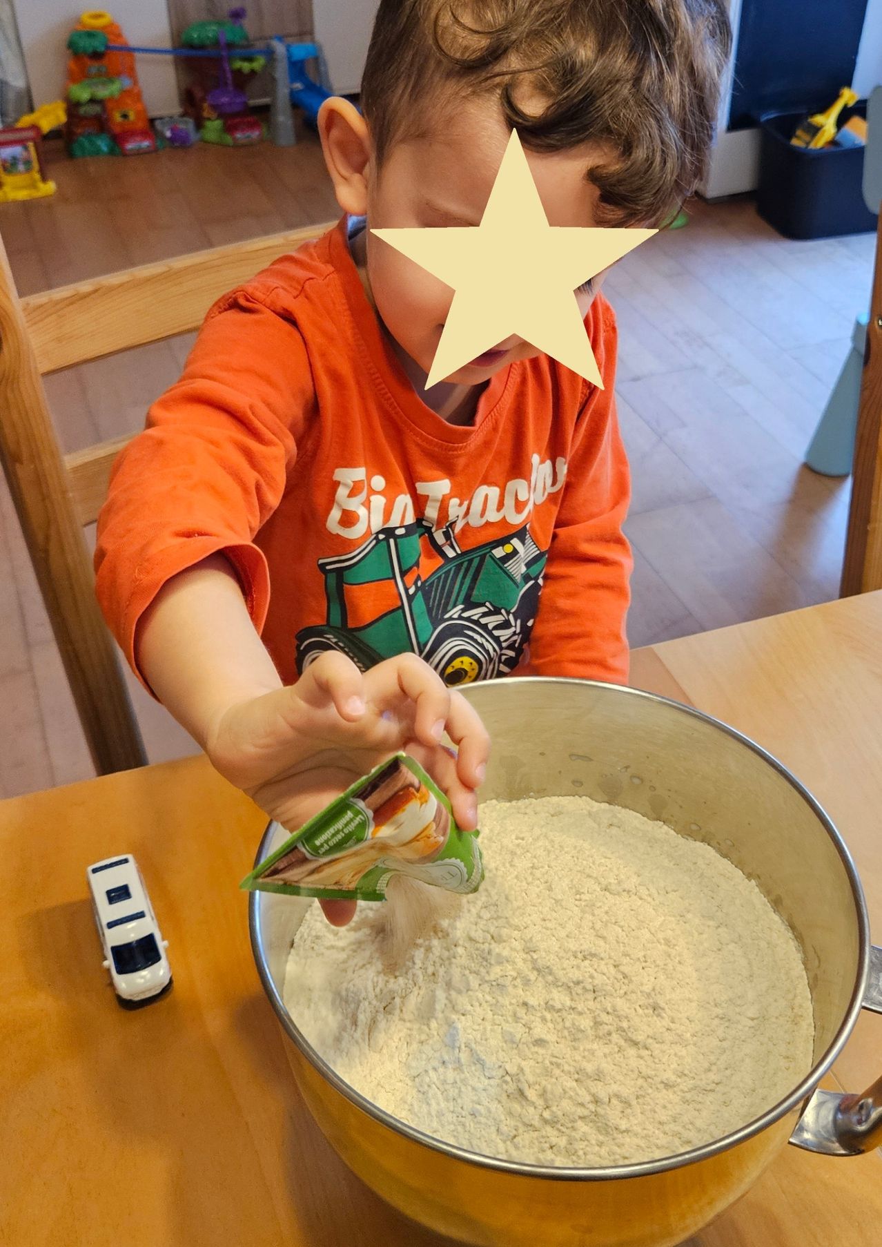 Ein kleiner Junge fügt eine Tüte Zutaten zu einer Schüssel Mehl auf einem Holztisch hinzu.