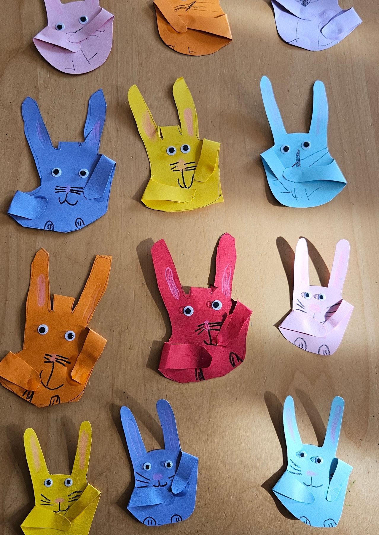Eine Sammlung von handgefertigten Papierhasen in verschiedenen Farben, einschließlich Blau, Gelb, Orange, Rot und Pink, auf einer Holzoberfläche platziert.