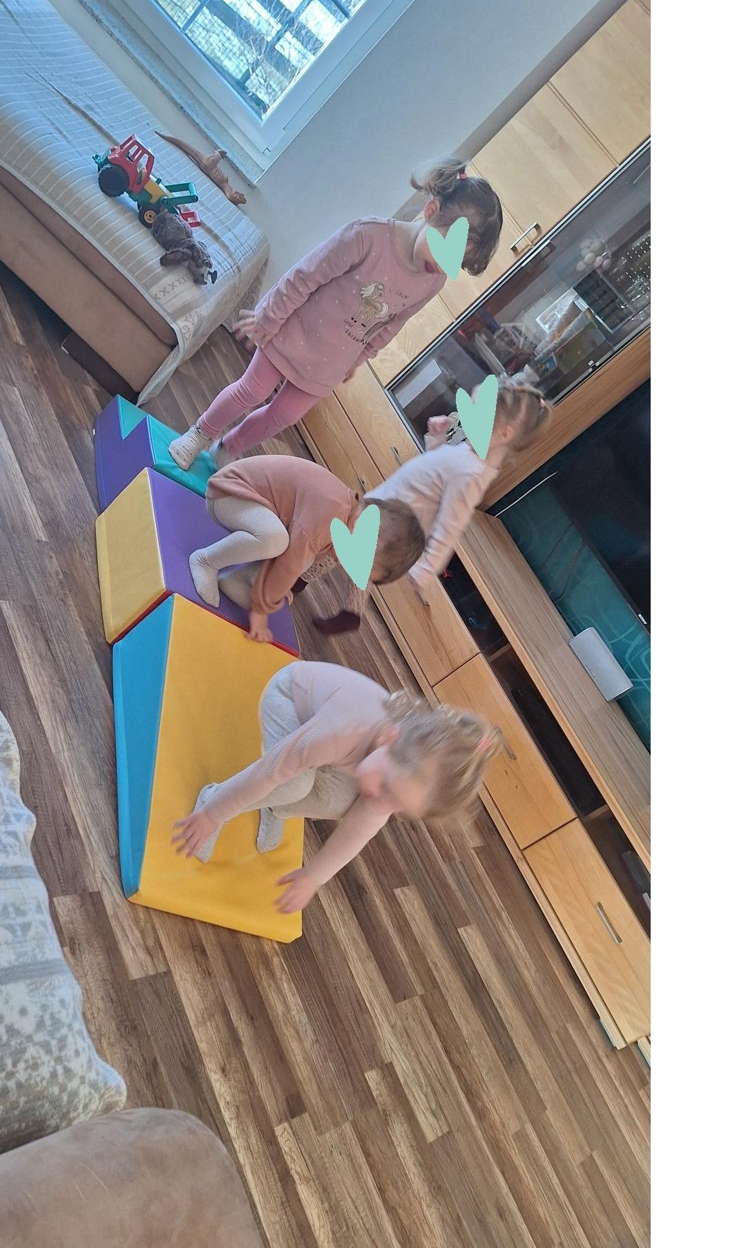 Vier kleine Kinder spielen in einem Wohnzimmer auf einem Set bunter Bausteine. Sie tragen rosa Kleidung.