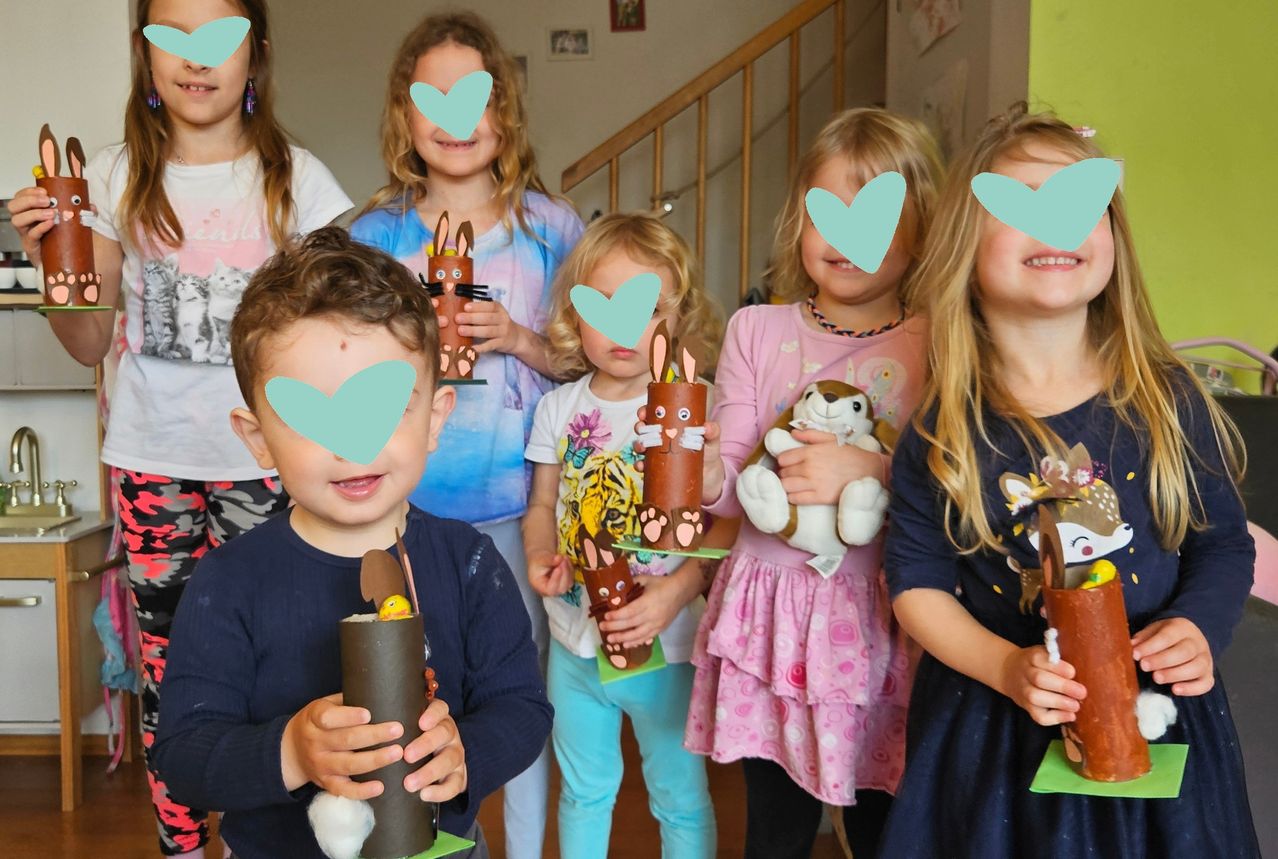 Mehrere Kinder stehen zusammen und halten dekorierte Tassen mit Hasen darauf. Sie scheinen an einer Bastelaktivität teilzunehmen. Herzen bedecken ihre Gesichter.