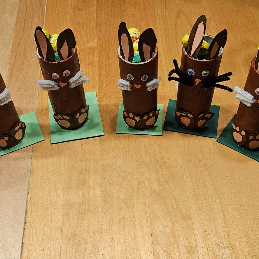 Fünf Osterbasteleien sind auf einer Holzoberfläche ausgestellt. Jedes Handwerk ist eine schokoladenfarbene Röhre mit einem Hasengesicht, gefüllt mit Süßigkeiten.